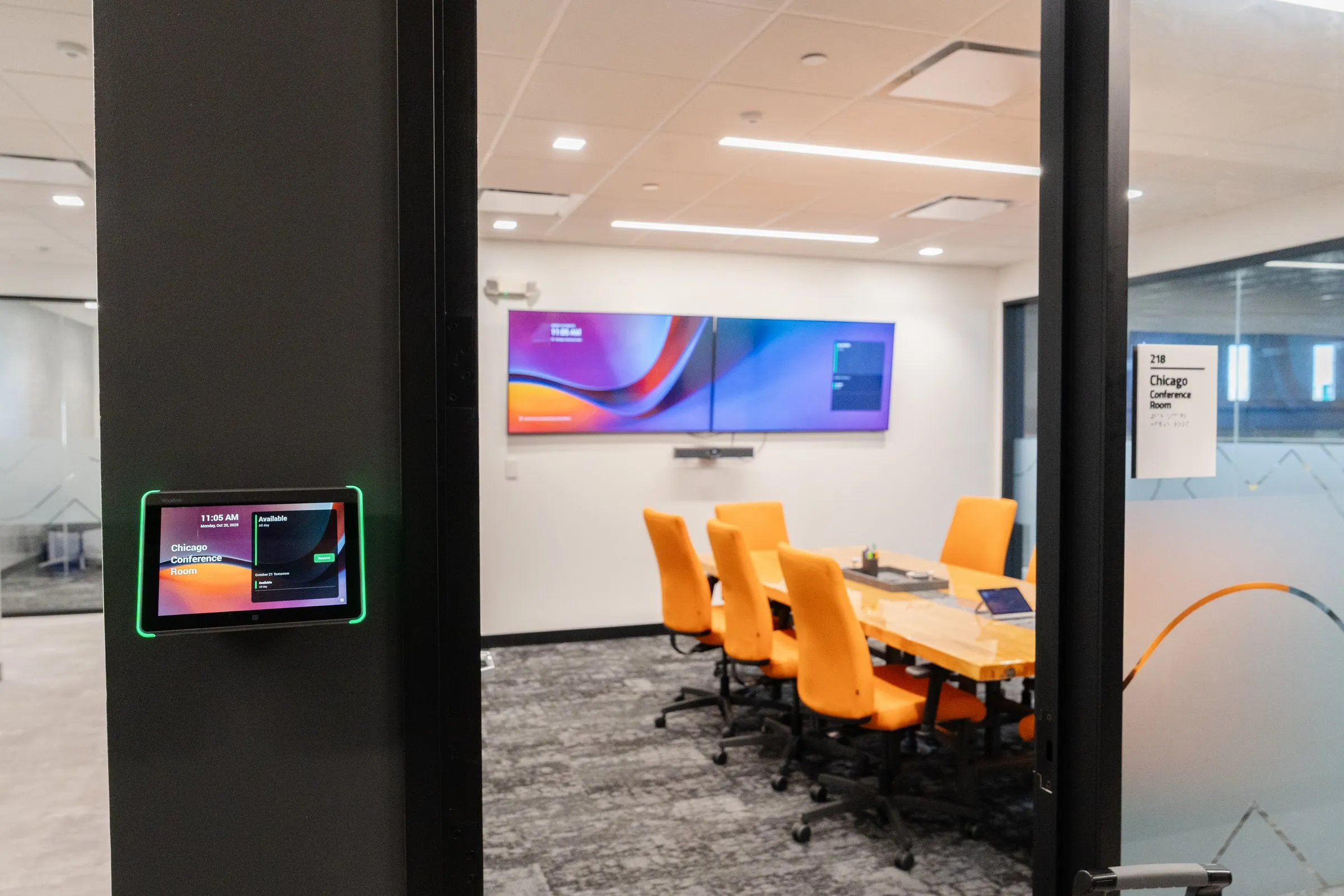 Conference room with dual displays and a room booking panel at the door